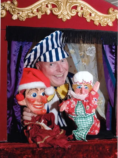 Martin Scott Price in his Punch & Judy booth holding Mr Punch & Judy puppets.